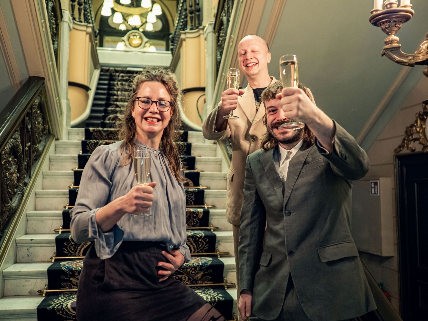 Drie mensen kijken naar de camera in nette kleding en champagne in hun handen