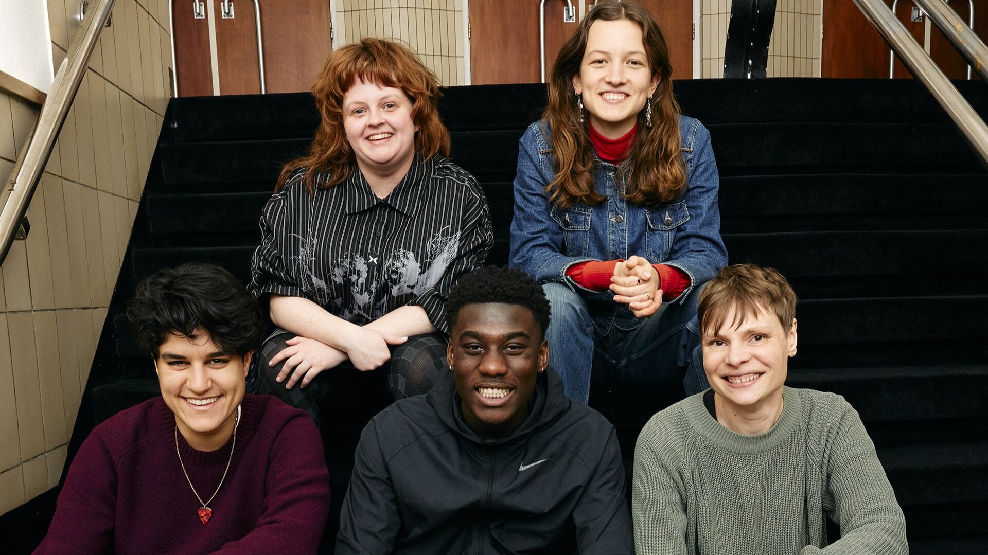 5 schrijvers zitten lachend op een trap 