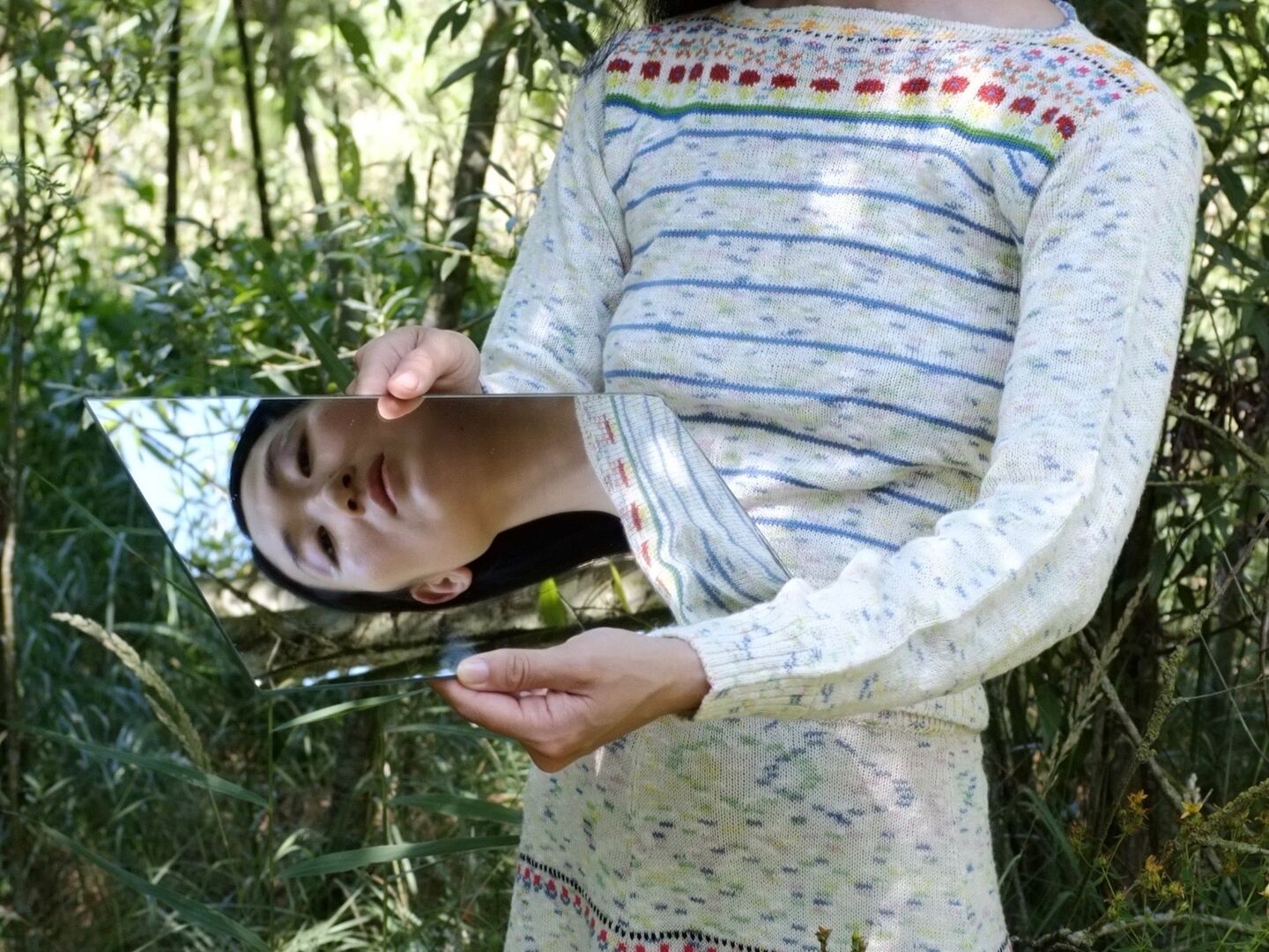 Het gezicht van een vrouw weerspiegelt op een spiegel zie zij vast houd, ze staat in de natuur