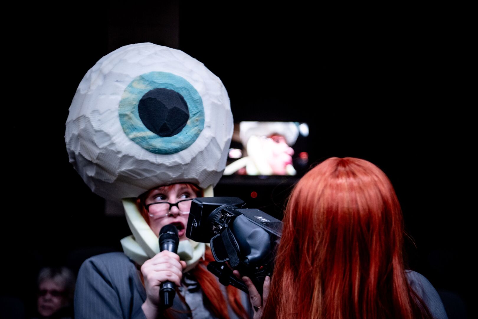 Een vrouw is aan het zingen in een microfoon met een groot oog op haar hoofd
